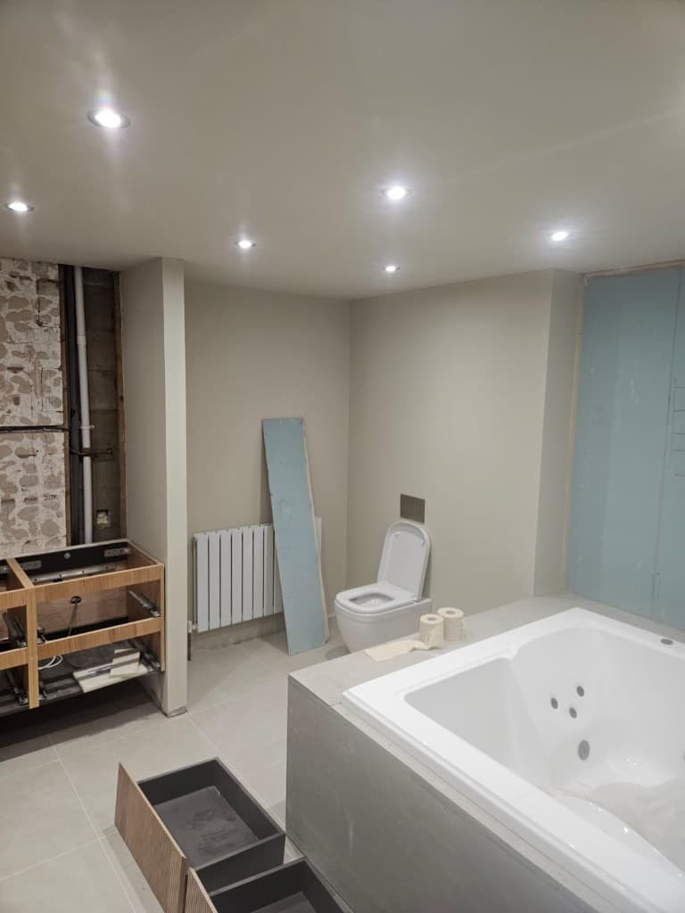 Bathroom renovation with freshly painted cream walls, a wall-hung toilet, white radiator and unfinished cabinetry.
